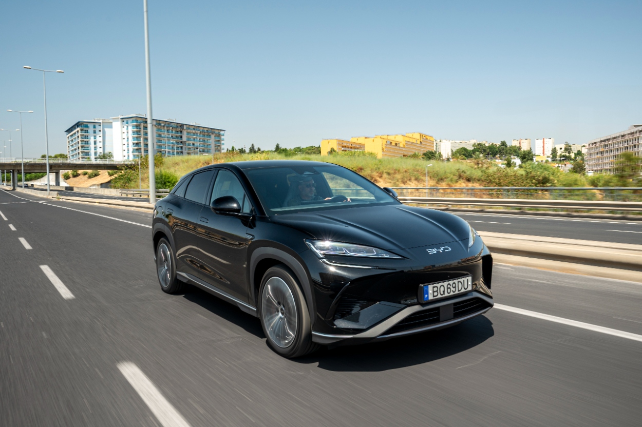 SUV moderno preto em movimento na estrada, com edifícios ao fundo. Design elegante e tecnologia avançada.
