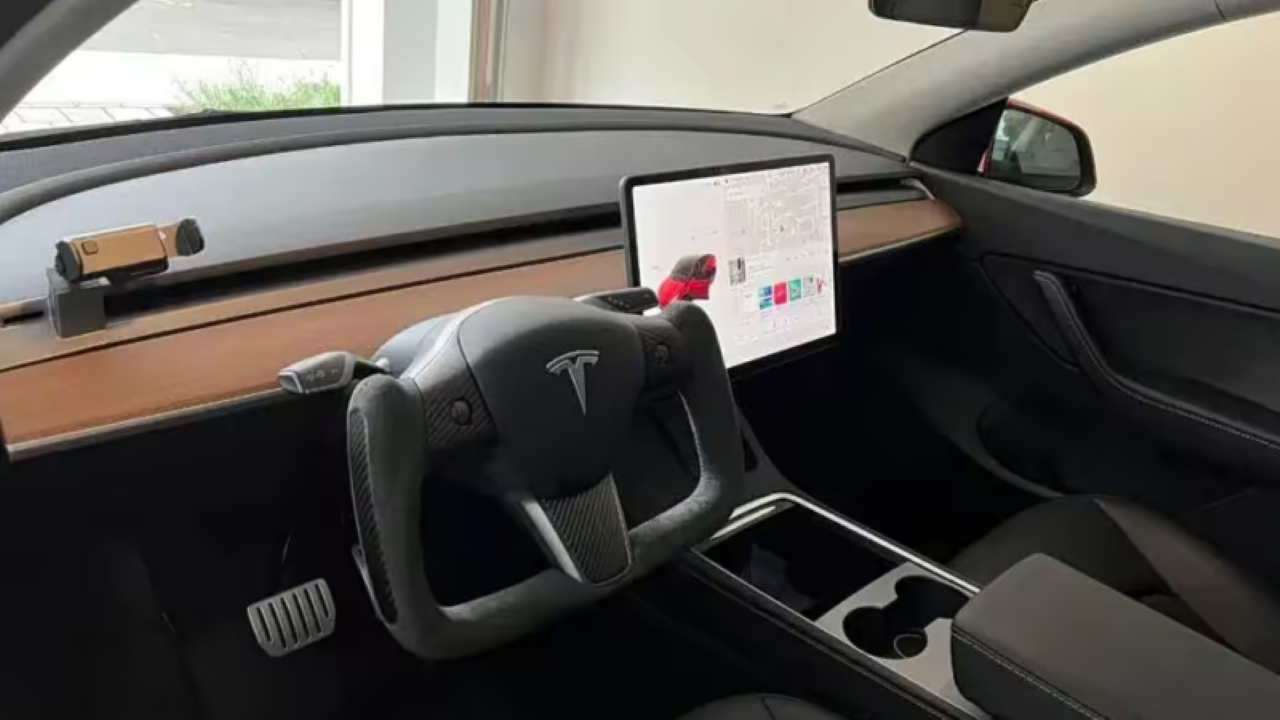 Interior moderno de um carro Tesla, com volante esportivo e painel digital exibindo informações do veículo.