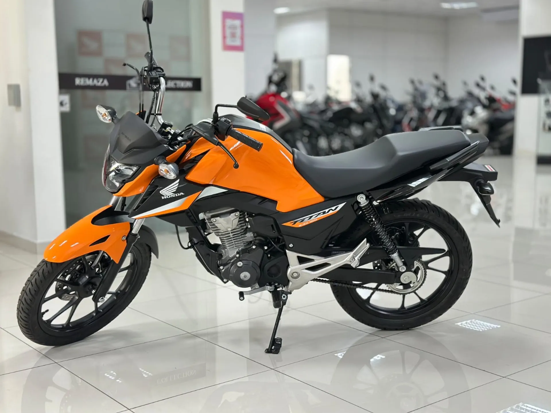 Moto Honda Titan laranja em concessionária, destacando design esportivo e moderno em ambiente iluminado.