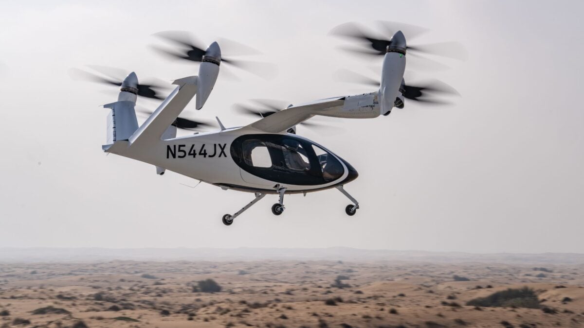 Helicóptero futurista em voo, com design inovador e rotores verticais, sobre um deserto árido.