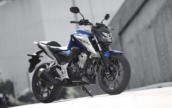 Moto Honda azul e branca em ambiente urbano, destacando seu design moderno e detalhes da mecânica.