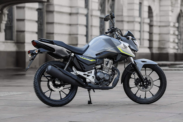 Moto Honda cinza estacionada em uma calçada, destacando seu design robusto e pneus all-terrain. Ideal para aventuras.